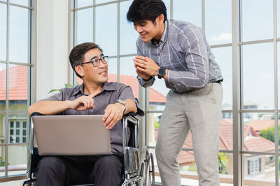 Businessman discussing over laptop with colleague while sitting on wheelchair