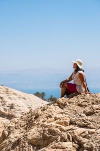  woman sits on rock at beach against clear sky