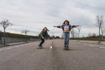 Female friends skateboarding on road against sky