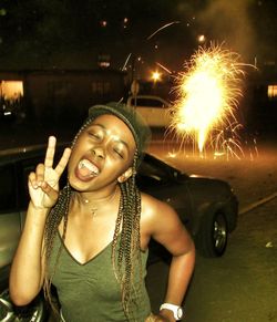 Young woman gesturing peace sign on street at night