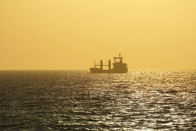 Ship sailing in sea against clear sky during sunset