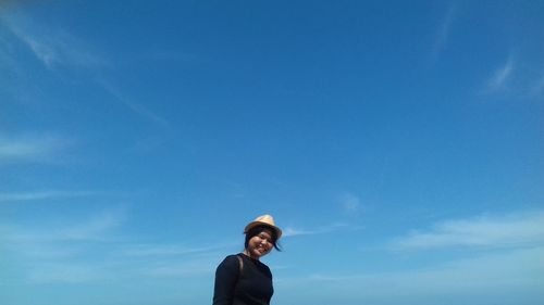 Low angle view of teenage girl standing against blue sky