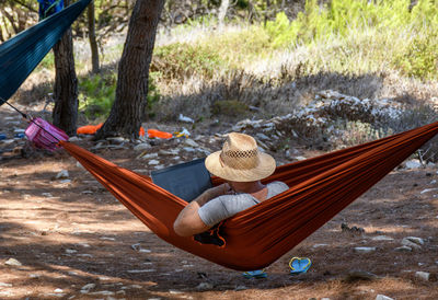 Rear view of man relaxing in hammock, using laptop computer