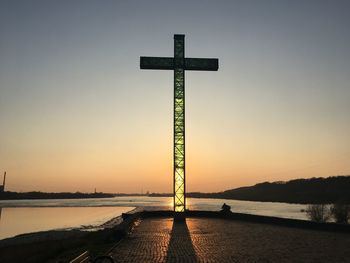 Cross on lake against clear sky during sunset