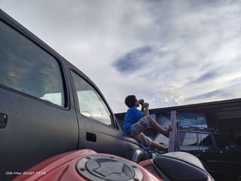 Man working on car against sky