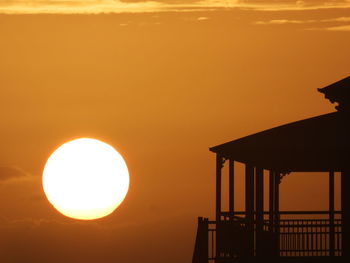 Silhouette built structure by sea against orange sky