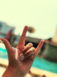 Cropped hand of woman gesturing horn sign against sky