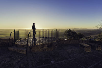 Silhouette man standing on observation point against clear sky during sunset