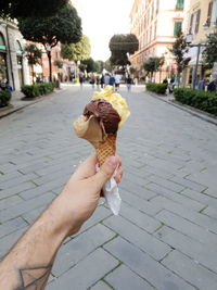 Cropped image of man holding ice cream cone on street