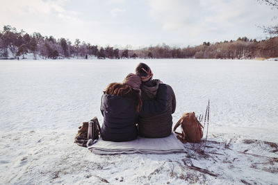 Rear view of male and female hiker sitting on snow covered field