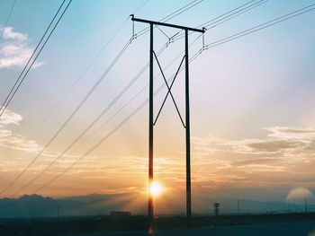 Low angle view of electricity pylon against sky during sunset
