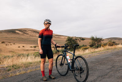 Full length of woman standing with bicycle on road