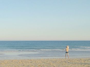 Rear view of woman standing on beach against clear sky