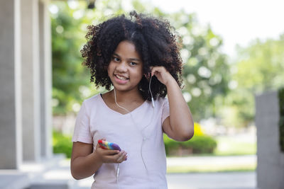 Portrait of smiling woman curly hair holding mobile phone outdoors