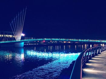 Illuminated bridge over river against clear blue sky at night