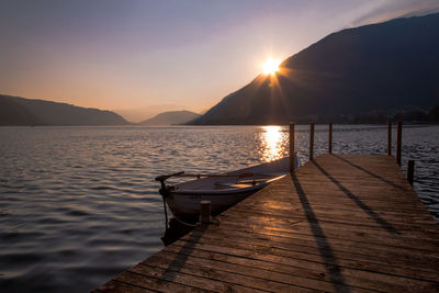 Boat moored by jetty in lake against sky during sunset