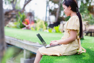 Side view of young woman using mobile phone in grass