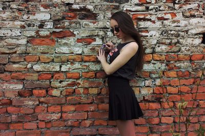 Side view of young woman standing by weathered brick wall