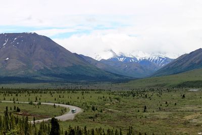 Scenic view of grassy field and mountain range against cloudy sky