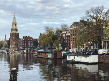 Sailboats in canal by buildings in city against sky