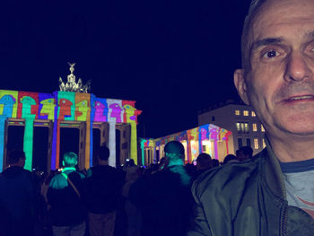 Portrait of woman with illuminated buildings against sky at night