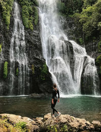 Full length of woman looking at waterfall in forest