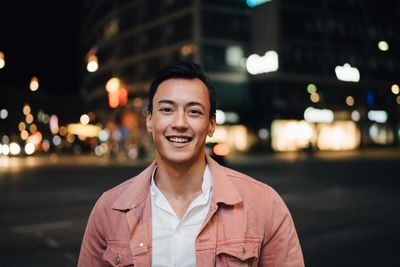 Portrait of smiling fashionable man standing in city at night