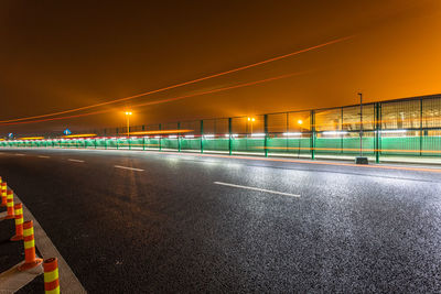 Empty road by illuminated city against sky at night