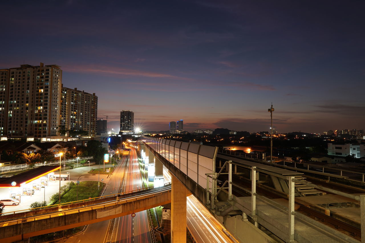 HIGH ANGLE VIEW OF LIGHT TRAILS ON ROAD AMIDST BUILDINGS