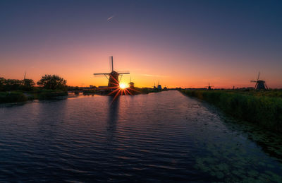 Traditional windmills by canal against sky during sunset