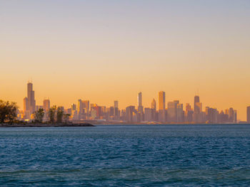 Sea and cityscape against clear sky during sunset