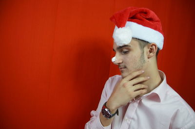 Thoughtful man wearing santa hat looking away against red background