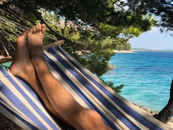 Low section of man relaxing on hammock at beach