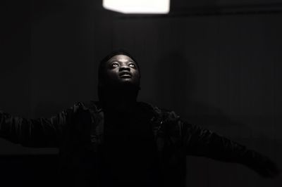 Young man standing below illuminated pendant light in darkroom