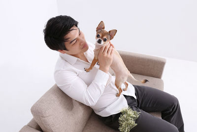 Man sitting with dog on sofa against white background