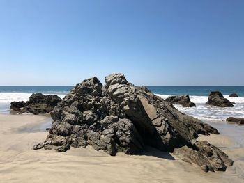 Scenic view of rocks on beach against clear sky