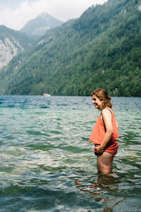 Side view of young woman standing on lake against mountains