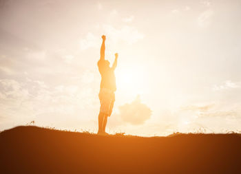 Silhouette woman with arms raised standing against sky during sunset