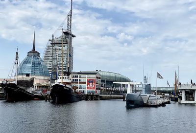 Sailboats moored on harbor by city against sky