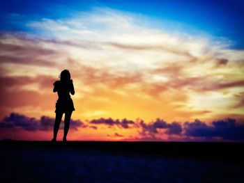 Silhouette woman photographing sea against sky during sunset