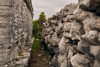 Stone wall by rocks against sky
