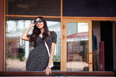 Woman with beautiful smile,  long dark hair near shop window. wearing sunglasses, polka dot dress