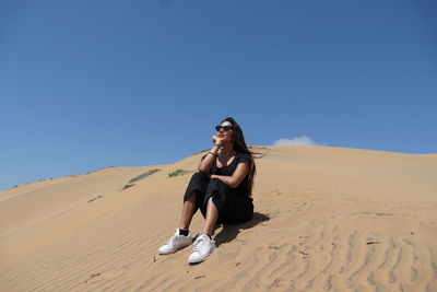 Full length of young woman wearing sunglasses against clear sky