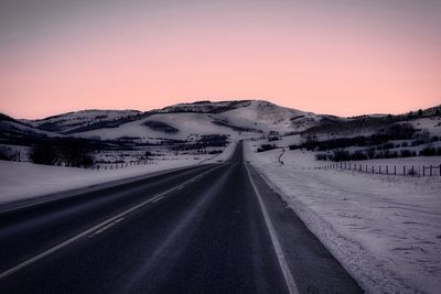 Road by mountains against clear sky during winter