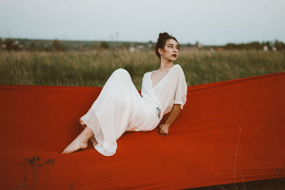 Thoughtful young woman sitting on hammock against sky