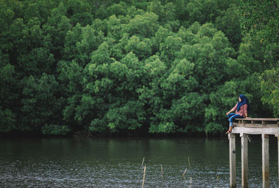 Young woman sitting by lake against trees