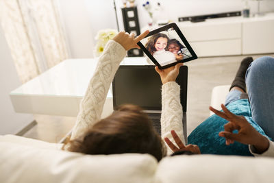 Smiling friends doing selfie while relaxing on sofa at home