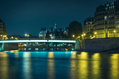 Illuminated bridge over river in city at night