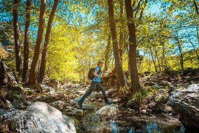 Active woman hiking jumping over a creek in spring