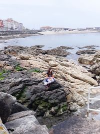 Woman sitting on rock by sea against sky